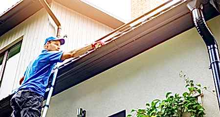 Man on a ladder inspecting his roof and rain gutters