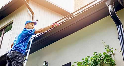 Man on a ladder inspecting his roof and rain gutters