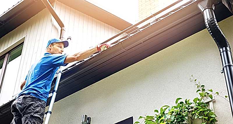 Man on a ladder inspecting his roof and rain gutters