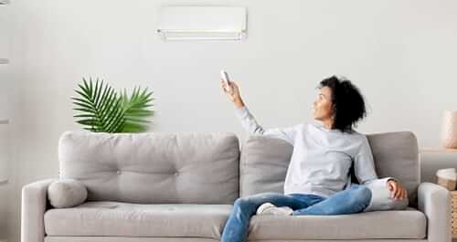 Woman sitting on couch pointing remote control at AC