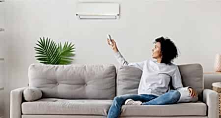 Woman sitting on couch pointing remote control at AC