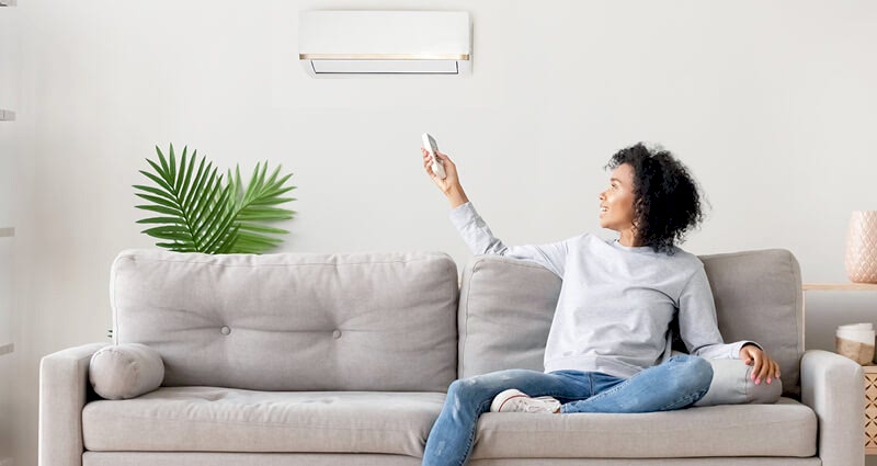 Woman sitting on couch pointing remote control at AC
